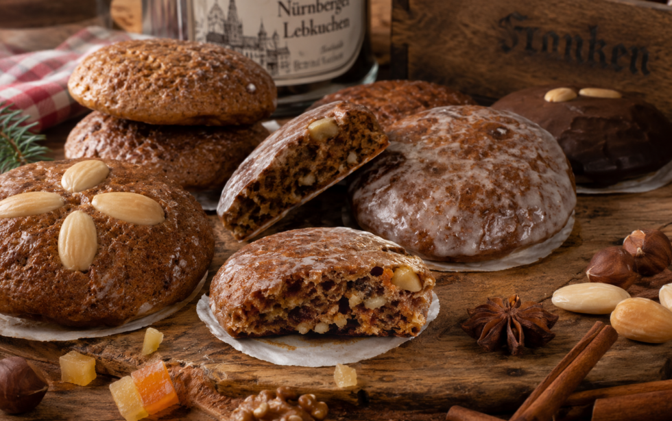 Fränkische Lebkuchen auf einem rustikalen Holztisch: verschiedene runde Lebkuchen mit Zuckerglasur und Mandeldekor, dazu Nüsse, kandierte Früchte, Zimtstangen und Sternanis.