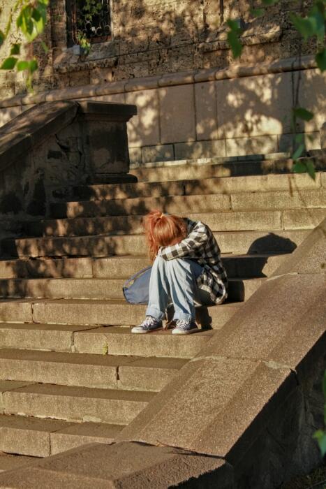 Eine junge Frau sitzt traurig auf einer Treppe.